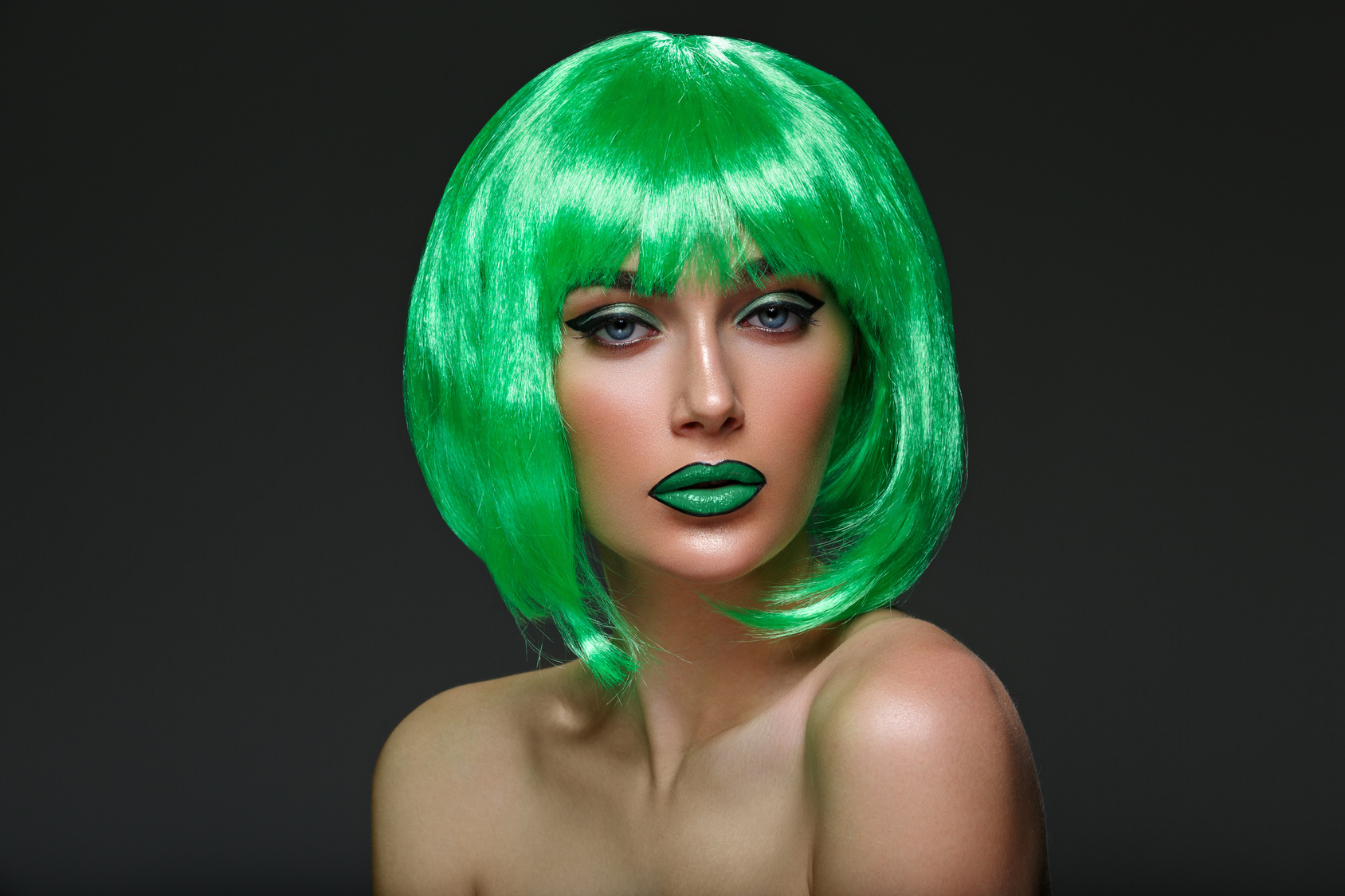 Beautiful young woman with glowing skin, fashion make-up in short green hair wig. Beauty shot on black background. Copy space.